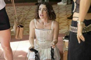 Szene aus der Serie: Maia sitzt im weißen Kleid auf dem Boden, vor ihr stehen zwei Personen, die nicht zu erkennen sind Szene aus der Serie: Maia sitzt im weißen Kleid auf dem Boden, vor ihr stehen zwei Personen, die nicht zu erkennen sind