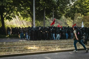 Menschen stehen während einer Demonstration eng zusammen und halten rote Fahnen in die Höhe