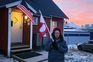 Eine Frau steht mit einer grönländischen Flagge vor einem roten Haus