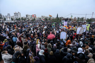 Sehr viele Menschen auf einem Platz. Sie halten Fahnen sowie Plakate mit den Fotos der Verstorbenen in die Höhe