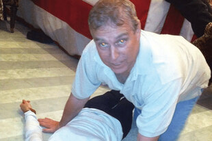 Ein Mann kniet auf dem Boden und beugt sich über eine Person.