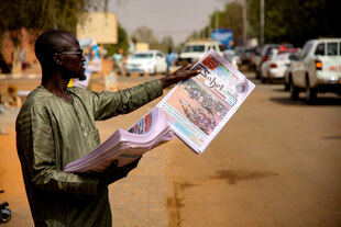 Ein Mann steht an einem Straßenrand und hält eine Tageszeitung in der Hand