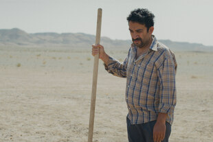 Ein Mann steht mit einem Stock in der Wüste.