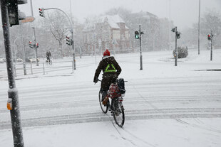 Ein Radfahrer überquert eine verschneite Fahrbahn