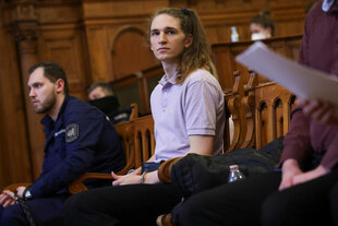 Eine angeklagte Person und Sicherheitspersonal sitzen in einem Gerichtssaal