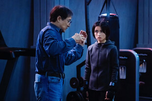 Jackie Chan und Zhang Zifeng stehen in einem Sportstudio zwischen Fitnessgeräten.