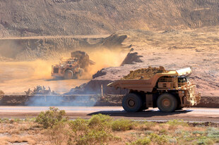 Muldenkipper und Bagger wirbeln Staub auf in einer Mine