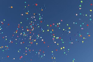 Ein Schwarm bunter Luftballons fliegt in einen blauen Himmel