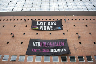 An der Außenwand der Elbphilharmonie hängen Kletterer Transparente auf, auf denen steht "Exit Gas" und "Neokolonialen Kapitalismus bekämpfen"