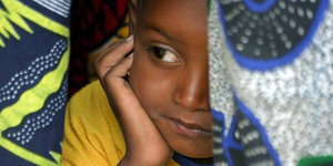 Ein Senegalesisches Mädchen schaut unter einem bunt gemusterten Tuch hervor