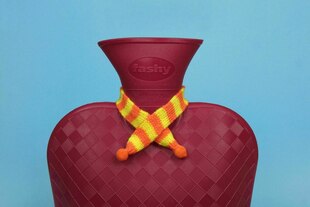 Dunkelrote Wärmflasche mit kleinen Schal, in einem Oval am Hals steht "Fashy"