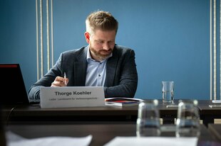 Thorge Köhler sitzt hinter einem Schild mit seinem Namen, gesenkten Kopfes