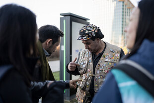 Ein Mann mit einer Jacke voller Pins, drei Menschen um ihn herum begutachten diese