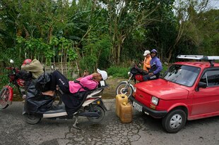 Ein rotes Auto, Motorräder und Benzinkanister an einem Straßenrand.