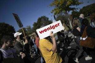 Eine protestierende Person hält ein Schild in die Höhe, auf dem steht: WENIGER