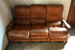 Dreiteiliges altes braunes Ledersofa steht in einer Ecke