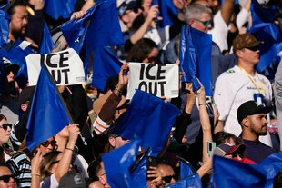 Menschen halten bei einem Footballspiel Schilder hoch mit dem Titel "ICE OUT"