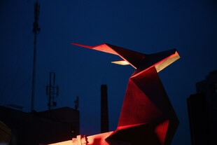 Rot angestrahlter Kopf eines Origami-Hirsches welcher sich vom dunkelblau bis schwarzen Nachthimmel abhebt