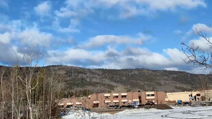 Eine Schule in einer Landschaft vor einem Hügel, Autos parken davor