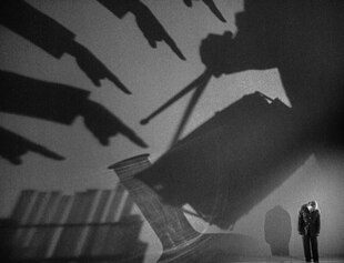 Ein Mann am rechten Bildrand unten blickt hinauf zu riesigen Schattenspielen.