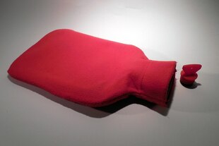 Eine rote Wärmflasche liegt mit geöffnetem Deckel auf weißem Grund
