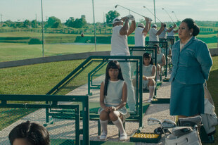 Eine Reihe von Frauen sitzt neben Golfern und legt diesen die Bälle zum Abschlagen vor.