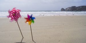 zwei kleine Plastikwindräder stecken im Sandstrand am Meer