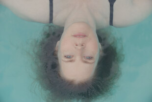 Eine Frau liegt über Kopf in einem Pool und blickt nach oben.