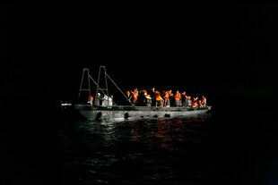 Ein Beiboot mit Menschen die orange Schwimmwesten tragen Mitten in der Nacht Ein Beiboot mit Menschen die orange Schwimmwesten tragen Mitten in der Nacht