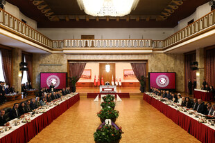 Ein altehrwürdiger Saal, mit zwei Seiten getrennt von Blumen, dahinter, hochgestellt eine Person am Tisch sitzend Ein altehrwürdiger Saal, mit zwei Seiten getrennt von Blumen, dahinter, hochgestellt eine Person am Tisch sitzend