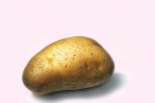 Eine gold schimmernde Kartoffel vor rosafarbenem Hintergrund