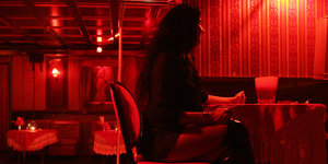 Eine Prostituierte sitzt in einem rot beleuchteten Raum an einem Tisch