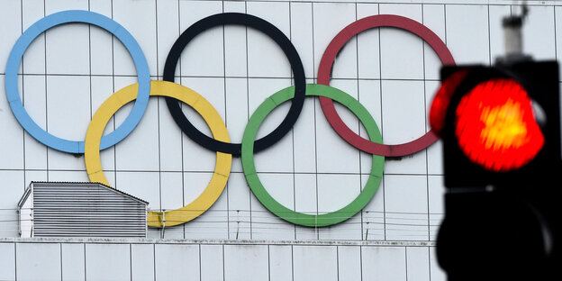 Die fünf Olympischen Ringe an einer Hauswand hinter einen roten Ampel