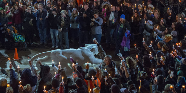 Mneschen stehen in einem großen Kreis und halten Kerzen, in der Mitte des Kreises eine Statue von einem Tier