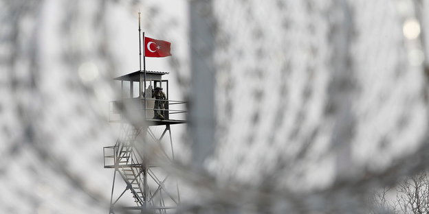 Durch Stacheldraht hindurch sieht man einen Wachturn mit türkischer Flagge