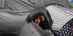 Ein Mensch schaut aus einem nassen, grauen Zelt hervor