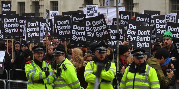 Menschen halten „Don't bomb syria“-Schilder, davor grinsende Polizisten