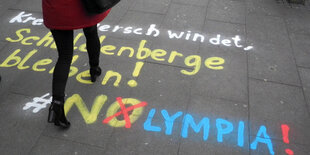 Eine Frau geht über eine mit Kreide gemalte Anti-Olympia-Parole.