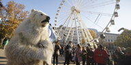 Ein Demonstrant im Eisbären-Kostüm steht vor einem Riesenrad