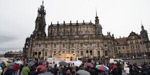 Menschen mit Regenschirmen stehen auf dem Theaterplatz in Dresden.