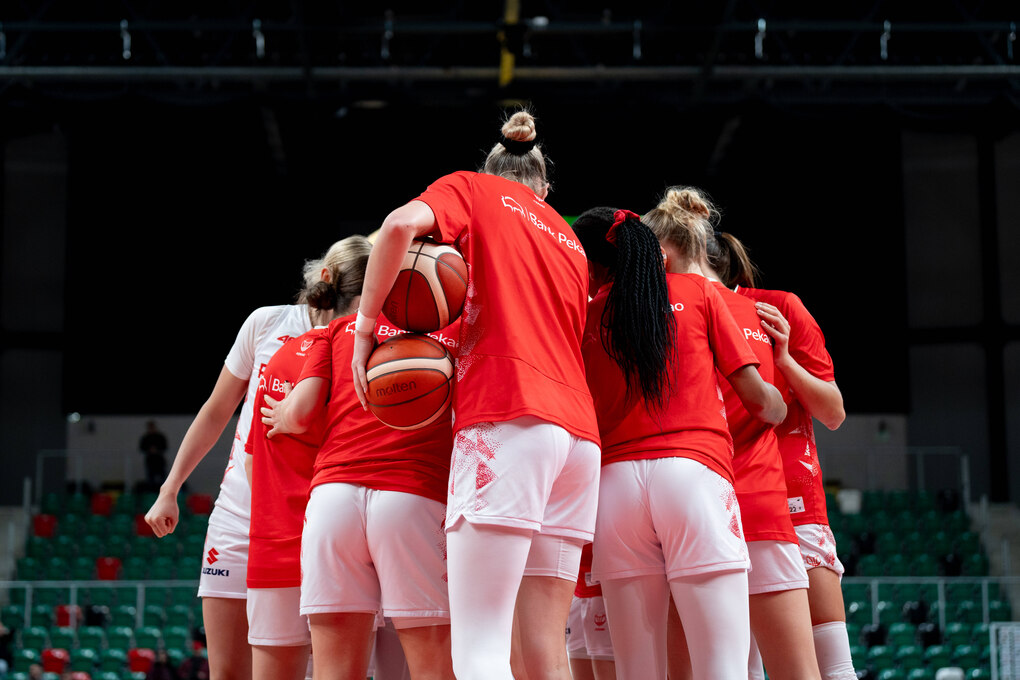 Basketballspielerinnen mit rotem Trikot stehen mit dem Rücken zur Kamera zusammen
