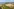 Eine Luftaufnahme zeigt eine weite Küstenlandschaft mit einem grünen Deich, Windkrafträdern und Marschwiesen, die im Hintergrund in das Stadtgebiet und die Hafenanlagen von Bremerhaven am Weserufer übergehen.
