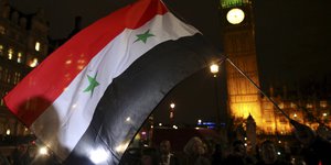Der Big Ben in London, es ist dunkel, im Vordergrund wird eine syrische Flagge geschwenkt