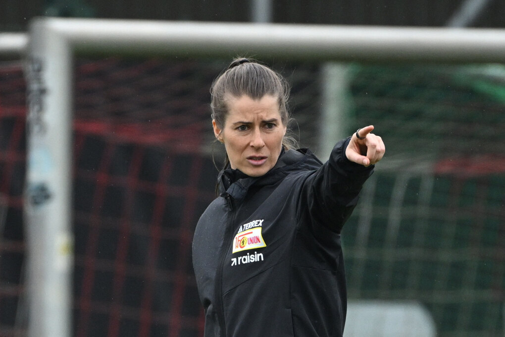 Marie-Louise Etat deutet mit dem Zeigefinger nach vorne. Hinter ihr ein Fußballtor.