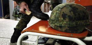 Bundeswehrsoldat, der seinen Stiefel auf einen Stuhl stellt, um mit der Bürste Schuhcreme zu verteilen.