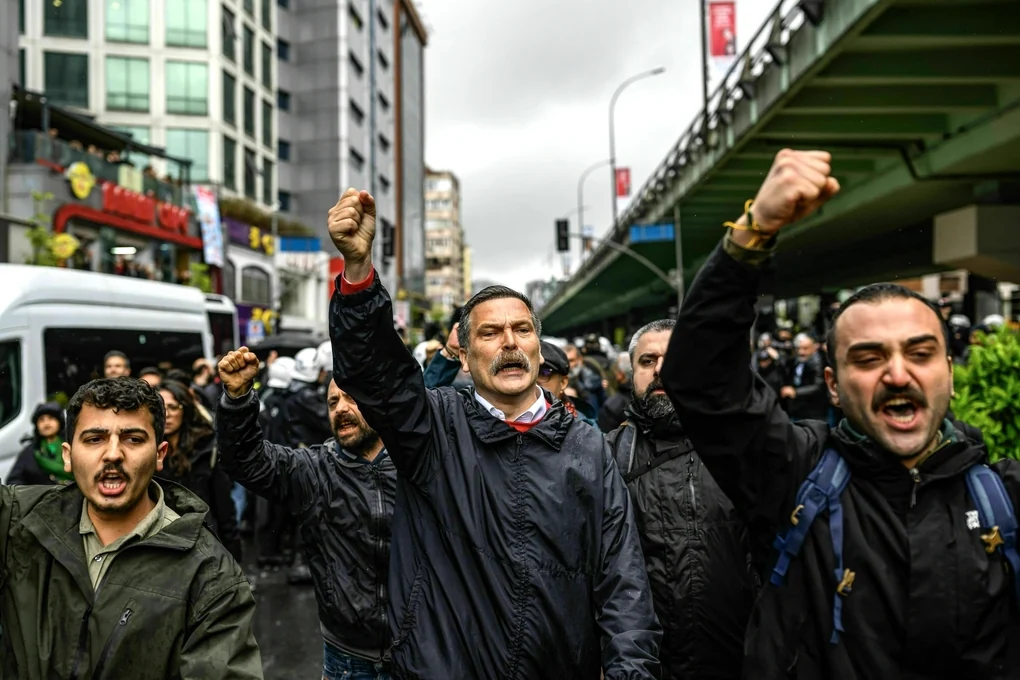 Erkan Bas spricht mit erhobener Faust bei einer Demonstration am 1. Mai, neben ihrm Männer, die auch die Faust erheben