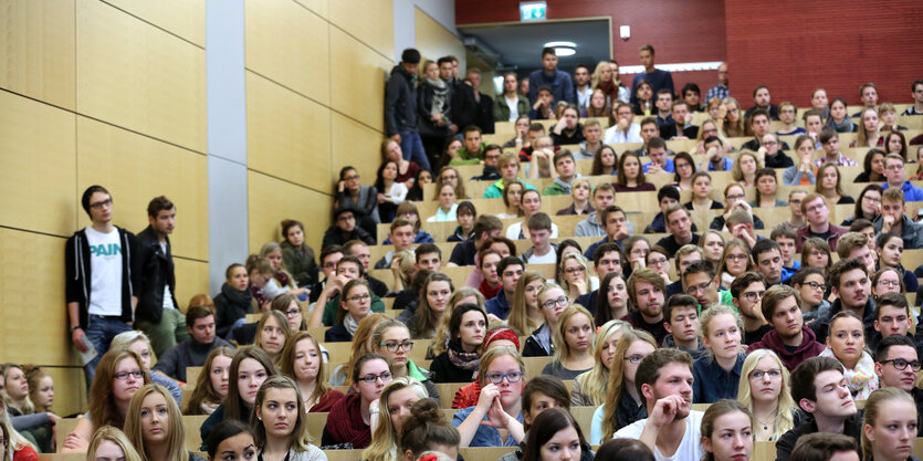 vollbesetzter Hörsaal in einer Uni, manche stehen sogar daneben