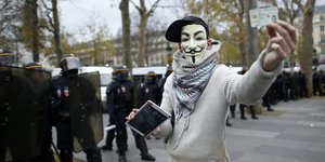Ein Demonstrant mit Guy-Fawkes-Maske hält einen Ausweis in die Kamera