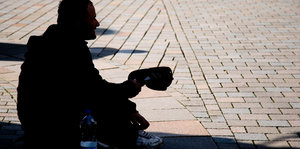 Ein Mann sitzt auf der Straße und bettelt, er ist von der Seite im Schatten zu sehen