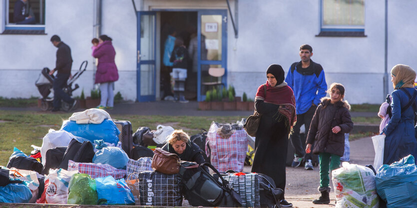 Menschen stehen vor einem Gebäude, Taschen und Gepäck liegen auf dem Boden